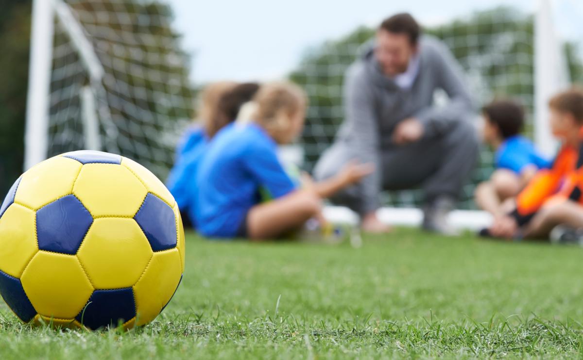 Voetbaltrainer met jonge voetballers, voetbal op de voorgrond