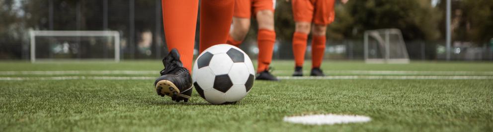 Voetballer in oranje tenue tikt bal aan.